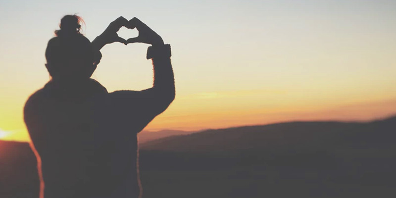 Silhoutted person making a heartshape with their hands